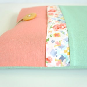 May include: A pink and mint green fabric laptop sleeve with a floral patterned fabric trim and a wooden button.