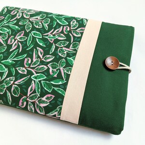 May include: A green and pink floral laptop sleeve with a beige flap and a wooden button closure.