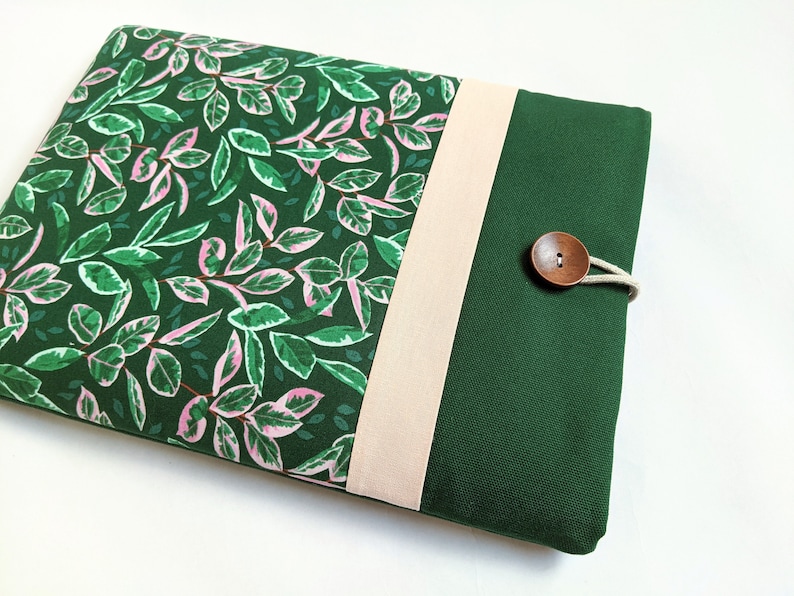 May include: A green and pink floral laptop sleeve with a beige flap and a wooden button closure.