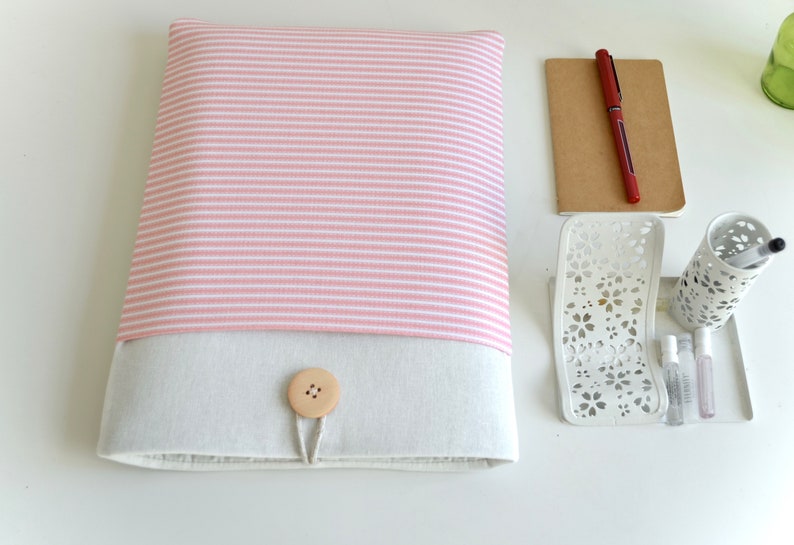 Op de afbeelding: Een roze en wit gestreepte laptophuls met een beige klep en een houten knoopsluiting.