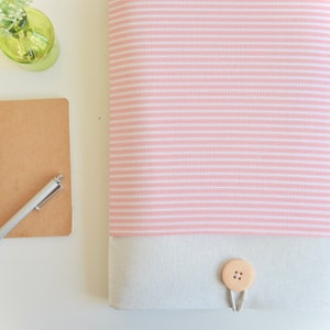 Op de afbeelding: Een roze en wit gestreepte laptophuls met een witte canvas klep en een houten knoopsluiting.