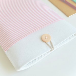 Op de afbeelding: Een witte laptophuls met een roze en witte gestreepte flap en een houten knoopsluiting.