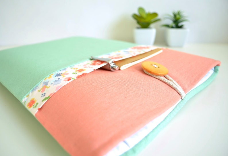 May include: A mint green and coral laptop sleeve with a floral patterned fabric detail and a brown button closure.