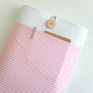 Op de afbeelding: Een roze en wit gestreepte laptophoes van stof met een witte klep van stof en een houten knoopsluiting.
