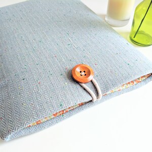 May include: A light blue laptop sleeve with a herringbone pattern and a wooden button closure. The sleeve has a floral lining.