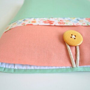 May include: A light green, pink, and white fabric laptop sleeve with a wooden button closure and a floral print.