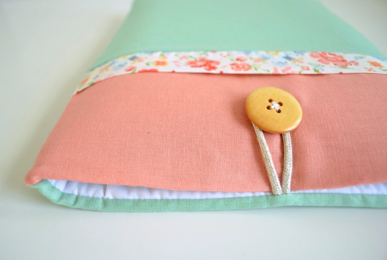 May include: A light green, pink, and white fabric laptop sleeve with a wooden button closure and a floral print.