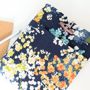 May include: A blue fabric pouch with a floral pattern in shades of yellow, orange, white, and green. The pouch has a flap closure with a wooden button.