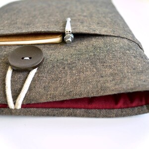 May include: A brown linen laptop sleeve with a red lining and a brown button closure. A notebook and pen are tucked into the pocket.