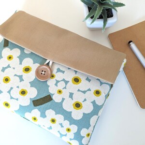 May include: A blue and white floral patterned laptop sleeve with a brown canvas flap and a wooden button closure.