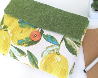 May include: A green and white fabric pouch with a lemon print and a wooden button closure. The pouch is folded over and has a green fabric lining.