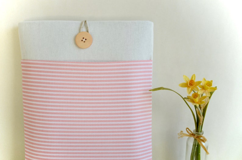 Op de afbeelding: Een roze en wit gestreepte laptophuls met een houten knoopsluiting.
