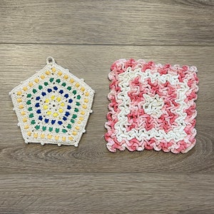 May include: Two crocheted pot holders, one is a geometric shape with a colorful center and the other is a square with a pink and white design.