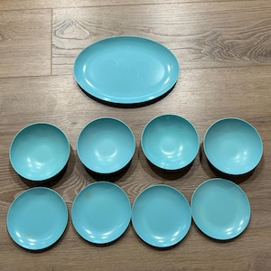 May include: A set of eight turquoise-colored dishes, including one oval platter and seven round bowls. The dishes are arranged on a wooden surface, showcasing their uniform color and design. The set is ideal for serving meals.