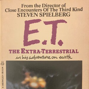 May include: A paperback book cover with a pink and white background. The title is "E.T. The Extra-Terrestrial" in his adventure on earth. The book is by William Kotzwinkle, based on a screenplay by Melissa Mathison.