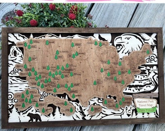 Puede incluir: Un mapa de madera de los Estados Unidos con árboles verdes que marcan la ubicación de cada parque nacional. El mapa está enmarcado en un marco marrón oscuro e incluye un águila, montañas y nubes. El texto "National Park Travel Map" y "Dane Powell" se incluye en la esquina inferior derecha.