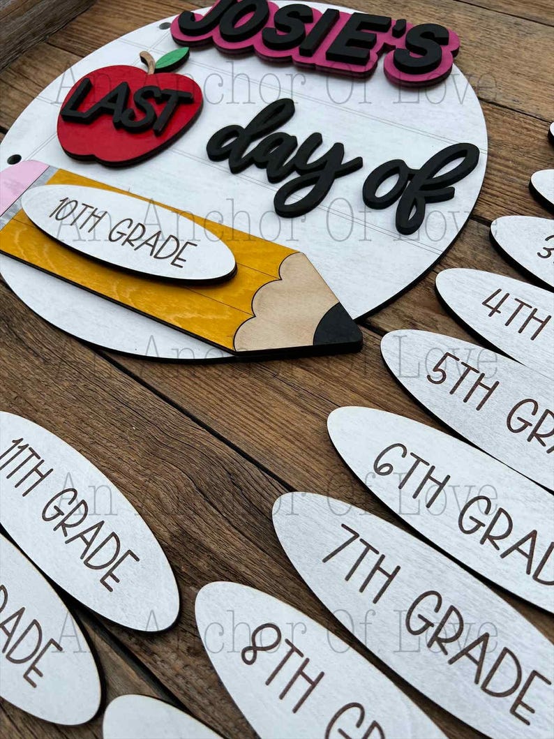May include: A wooden school-themed sign with the text "Josie's Last Day of" and a pencil, apple, and grade level markers. The sign is white with black and red accents. Grade levels include 10th, 11th, 3rd, 4th, 5th, 6th, 7th, and 8th grade.
