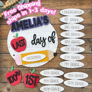 May include: A wooden school-themed sign with the text "AMELIA'S day of" and a pencil, apple, and grade level options. The sign includes the text "LAST" and "PRESCHOOL". Additional apple cutouts display "100th" and "1st".