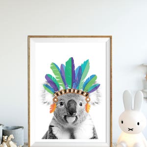 Puede incluir: Una foto en blanco y negro de un koala con un tocado de plumas de colores. El koala est&aacute; mirando directamente al espectador.