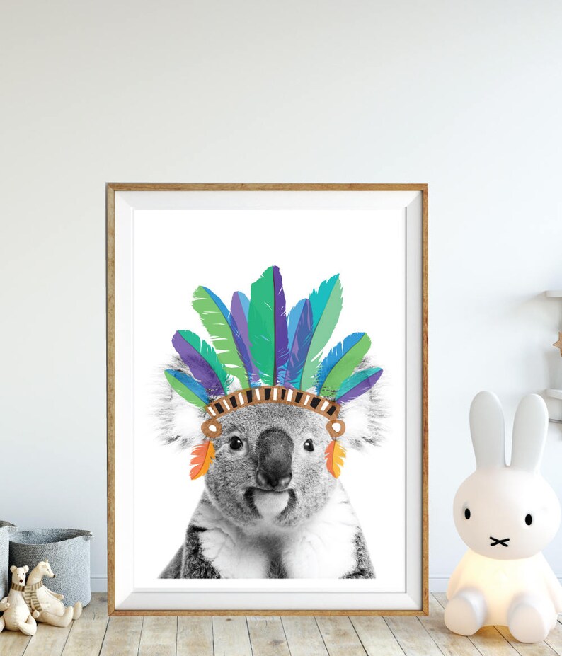Puede incluir: Una foto en blanco y negro de un koala con un tocado de plumas de colores. El koala est&aacute; mirando directamente al espectador.