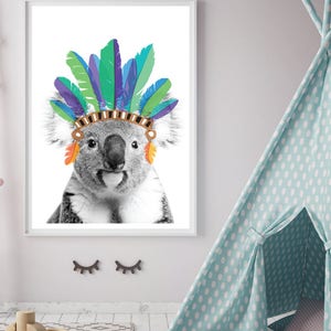 Puede incluir: Una foto en blanco y negro de un koala con un tocado de plumas de colores. El koala mira directamente a la c&aacute;mara con una expresi&oacute;n seria.