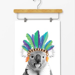 Puede incluir: Una foto en blanco y negro de un koala con un tocado de plumas de colores. El koala est&aacute; mirando directamente al espectador.