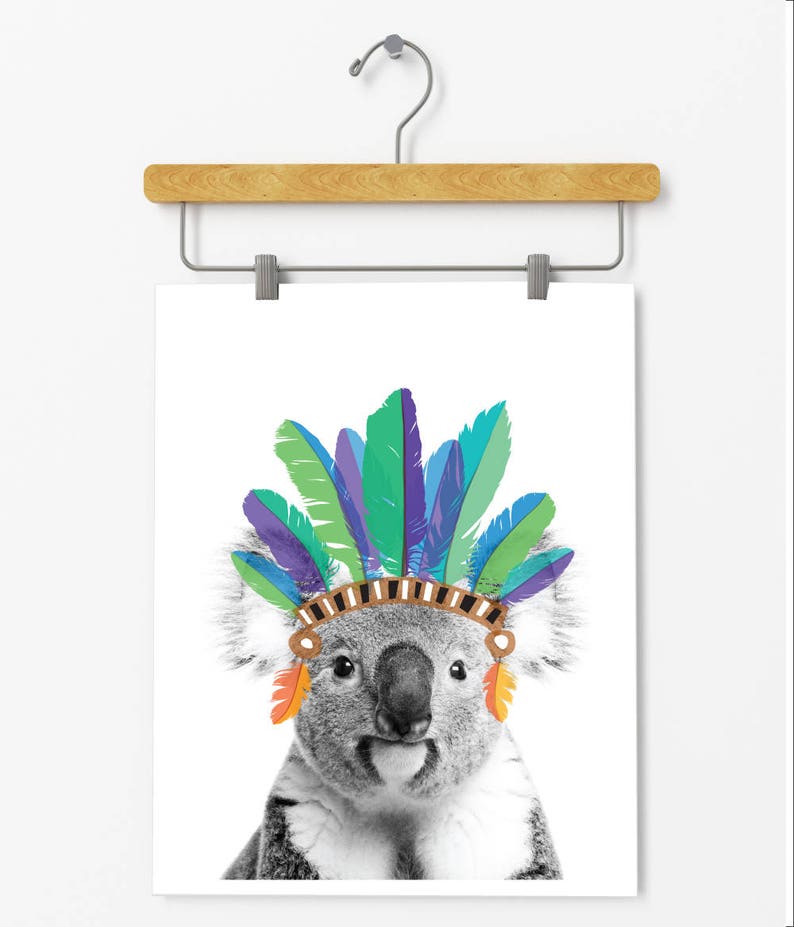 Puede incluir: Una foto en blanco y negro de un koala con un tocado de plumas de colores. El koala est&aacute; mirando directamente al espectador.
