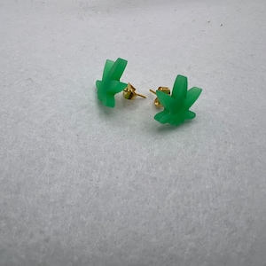 Peut inclure: Une paire de boucles d'oreilles clous en forme de feuille de marijuana verte avec des tiges dorées.