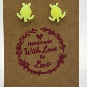May include: A pair of yellow flower-shaped stud earrings on a brown card with the text "Handmade With Love By Lena".