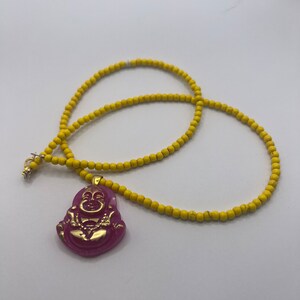 May include: A yellow beaded necklace with a pink and gold Buddha pendant.