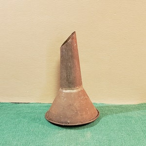 Könnte beinhalten: Ein antiker Trichter aus Metall mit einer breiten Basis und einem schmalen Auslauf. Der Trichter ist rostig und hat ein abgenutztes, altes Aussehen.