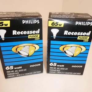 May include: Two black and blue Philips boxes for 65-watt recessed flood lights. Each box features a yellow and silver light fixture graphic, the Philips logo, and the text "Recessed Flood 120V". The boxes also state "Indoor" and include light bulb specifications.