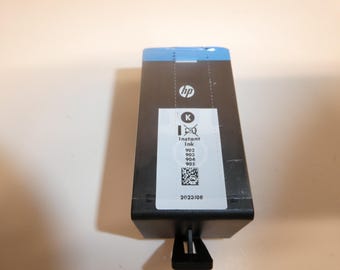 May include: A black HP Instant Ink cartridge with a blue top. The cartridge has a white label with the HP logo, the word "Instant Ink", and the numbers 902, 903, 904, and 905. The expiration date is 2023/08.