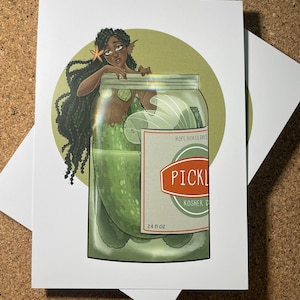 Puede incluir: Una sirena verde con el pelo largo y negro está atrapada dentro de un frasco de vidrio lleno de pepinillos. El frasco tiene una etiqueta roja y blanca que dice "HOPE HOKULANI PICKLES KOSHER DILL 24 fl oz".