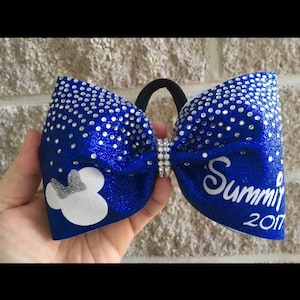 May include: A royal blue cheer bow with silver glitter and rhinestones. The bow has a white Mickey Mouse silhouette on one side and the text "Summit 2017" on the other side.
