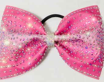 May include: A large, bright pink hair bow with a sparkling rhinestone design. The bow is embellished with numerous clear rhinestones and has a black elastic band. The center of the bow features a rhinestone band.