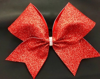 May include: A large red glitter cheer bow with a white rhinestone center.