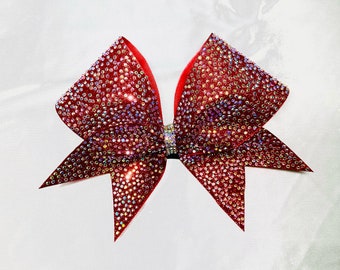 May include: A large red cheer bow with iridescent rhinestones. The bow is made of a soft, shiny fabric and has a pointed shape.