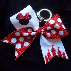 May include: Red and white bow with white polka dots and glitter. The bow features a black and white Minnie Mouse silhouette on one side and a red glitter castle silhouette on the other. The bow is attached to a silver key ring.