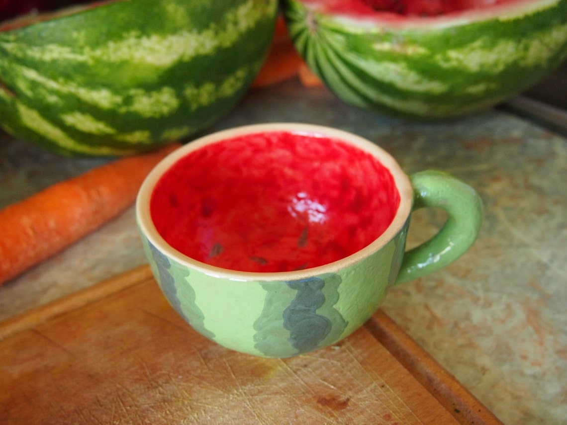 May include: A green and red ceramic mug shaped like a watermelon with a red interior and a green handle.