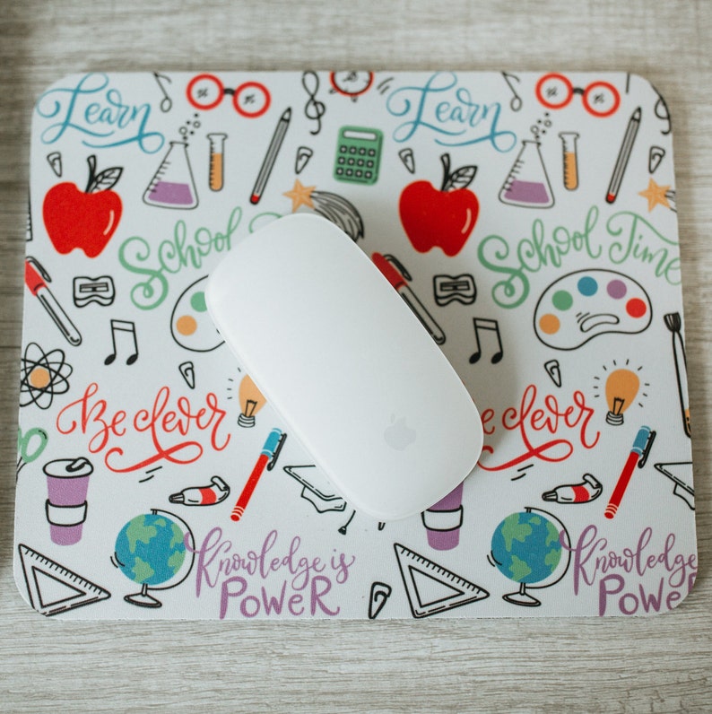May include: A white mouse pad with a colorful school-themed design. The design includes images of pencils, paintbrushes, musical notes, and the words "Learn", "School Time", "Be Clever", and "Knowledge is Power".