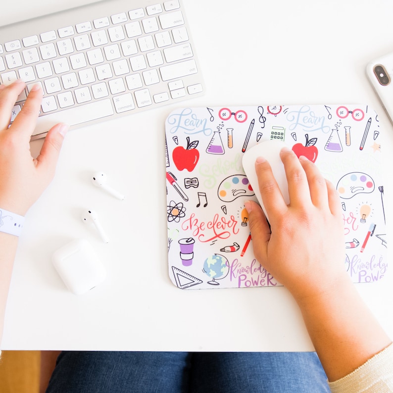 May include: A white mousepad with a colorful design featuring doodles of school supplies, a globe, and the words "Learn", "Be Clever", and "Knowledge is Power".