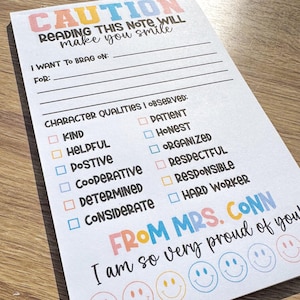 Puede incluir: Una nota imprimible colorida con el texto "CAUTION READING THIS NOTE WILL make you smile" y una lista de verificaci&oacute;n de cualidades de car&aacute;cter. La nota est&aacute; firmada "FROM MRS. CONN I am so very proud of you" e incluye una fila de caras sonrientes.