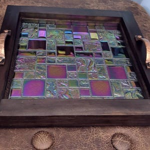 May include: A decorative serving tray with a dark wooden frame and copper-colored handles. The tray's surface is a mosaic of iridescent glass tiles in shades of purple, green, and blue, creating a colorful and textured design.