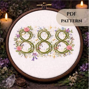Puede incluir: Un bastidor de bordado con un diseño de punto de cruz del número 888, adornado con vides verdes, rosas rosas y flores moradas. El texto "PDF PATTERN" es visible. El bastidor se encuentra sobre un fondo de velas y follaje.