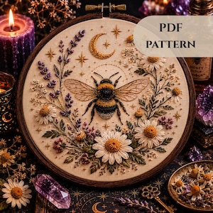 Puede incluir: Un bastidor de bordado circular que contiene un panel de tela con un diseño bordado detallado de un abejorro central rodeado de ramas de lavanda, margaritas blancas y una luna creciente dorada con estrellas. El texto PDF PATTERN es visible.
