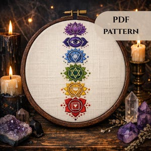 May include: An embroidered hoop art piece displaying the seven chakra symbols in various colours. The design includes a purple lotus flower, an eye, and geometric shapes. The text "PDF PATTERN" is visible. The hoop is set against a backdrop of candles and crystals.