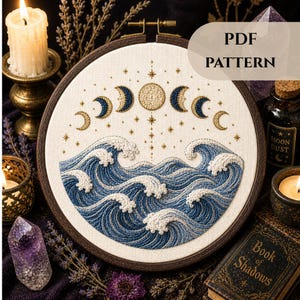 May include: A PDF embroidery pattern featuring a celestial design with moon phases and ocean waves. The design is stitched in shades of blue and gold on a cream-colored fabric, set in a wooden embroidery hoop. The text "PDF PATTERN" is visible.