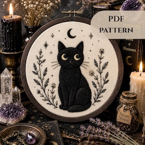 May include: A black cat embroidery design in a wooden hoop. The cat has golden eyes and sits beneath a crescent moon and stars. The text "PDF PATTERN" is visible. The design is surrounded by floral and botanical elements.