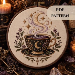 Könnte beinhalten: Ein Stickrahmen mit einem Stoffeinsatz, der eine Teetasse auf einer Untertasse zeigt. Die Tasse ist dunkel mit einem goldenen Halbmond und Blumenmotiven. Wirbelnder Dampf steigt zu einem Halbmond und Sternen auf. Der Text lautet PDF PATTERN.